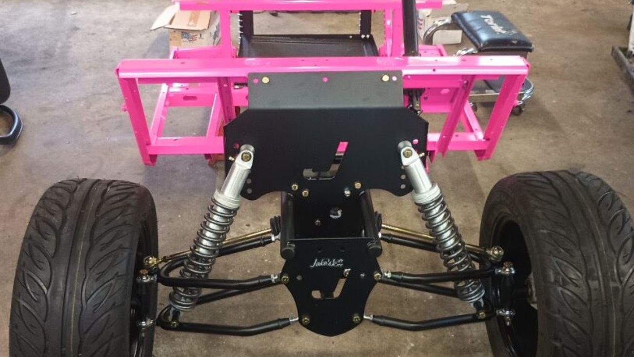 Custom golf cart frame with pink powder coating and suspension components.