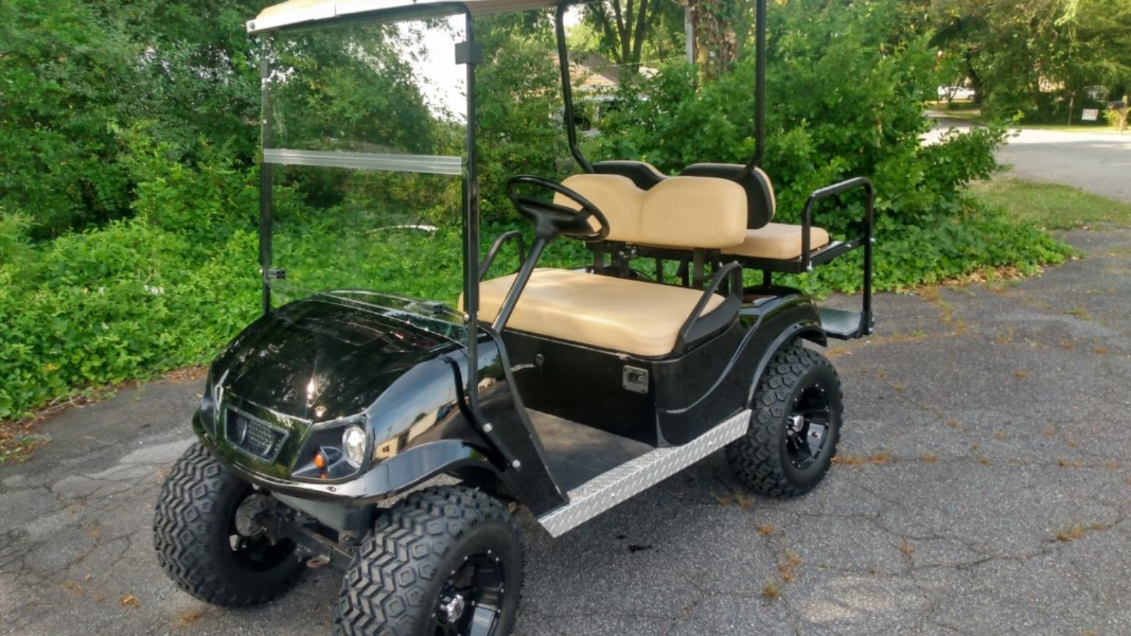 Customized black golf cart with tan seating and upgraded wheels